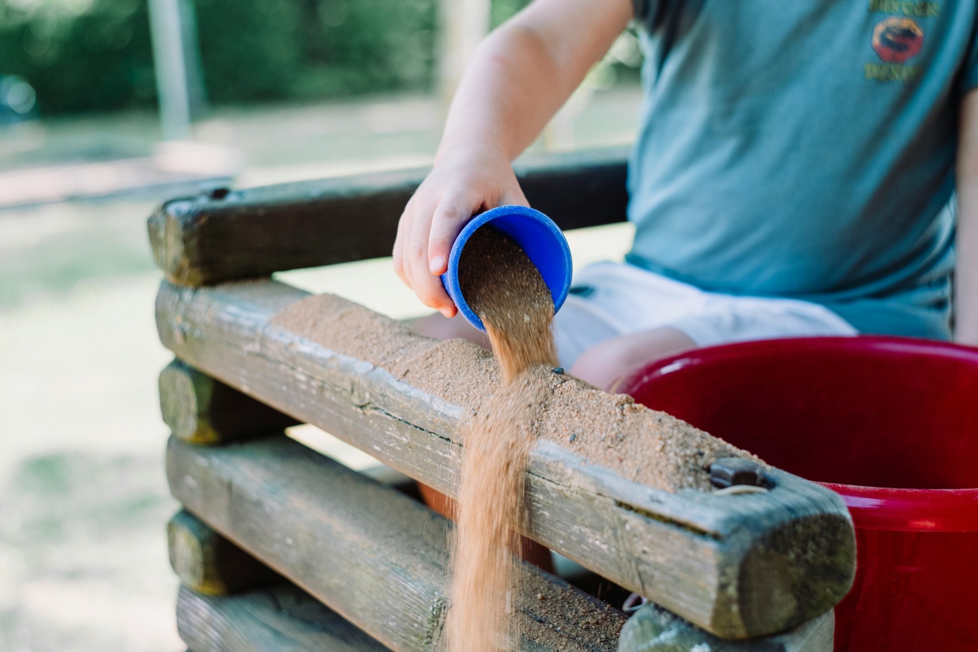 toddler pouring sand in a wooden outdoor sensory play area